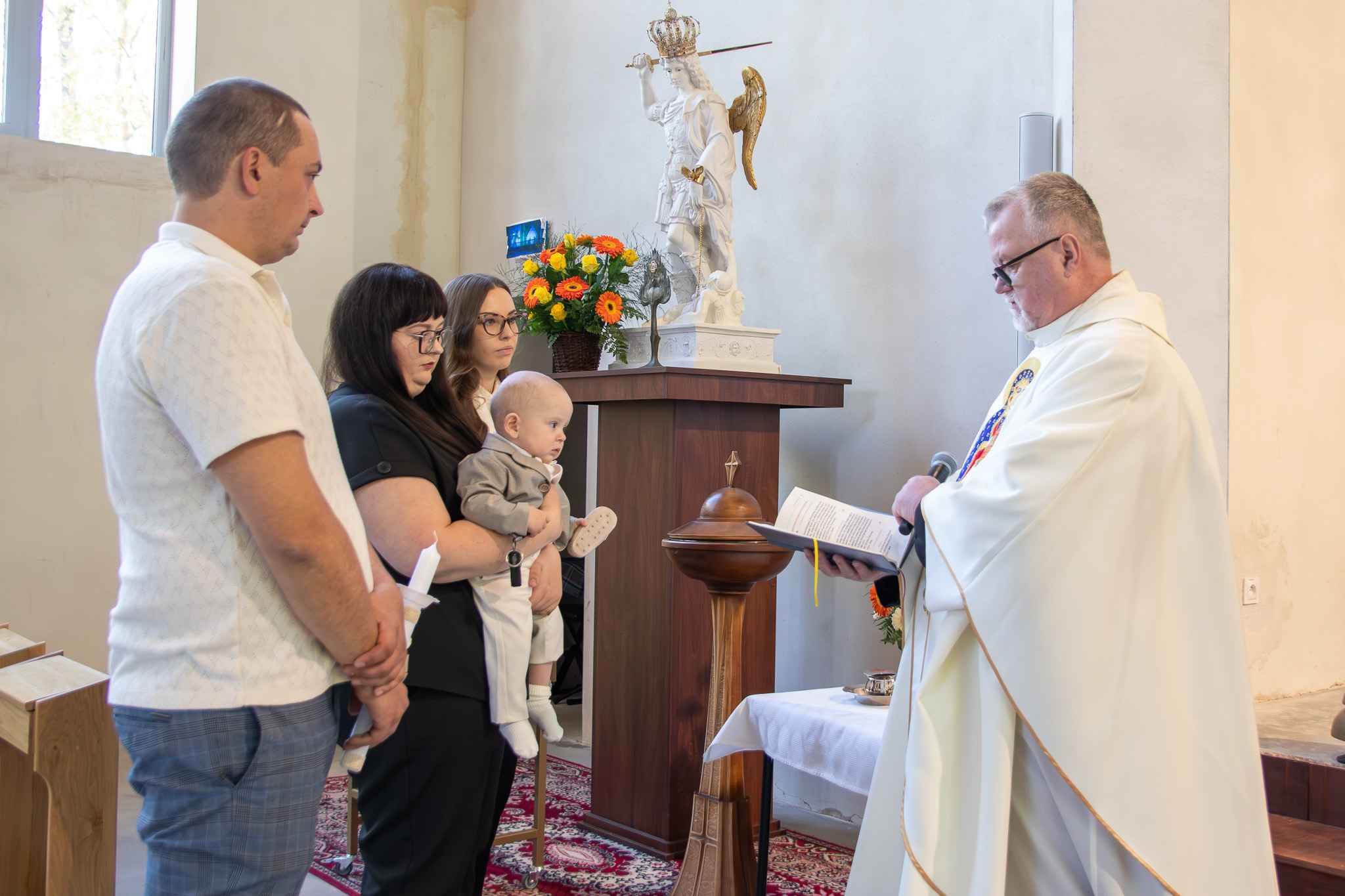 mama z chrzestnymi oraz dzieckiem stoją na przeciwko księdza