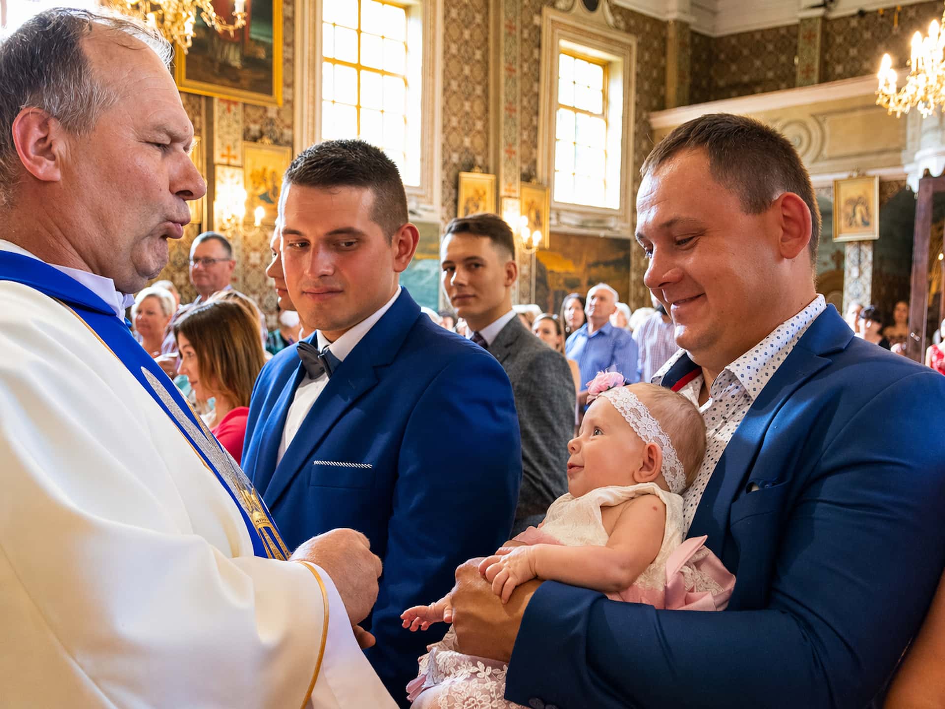 Udzielanie sakramentu chrztu świętego — interakcja księdza z dzieckiem i rodzicami