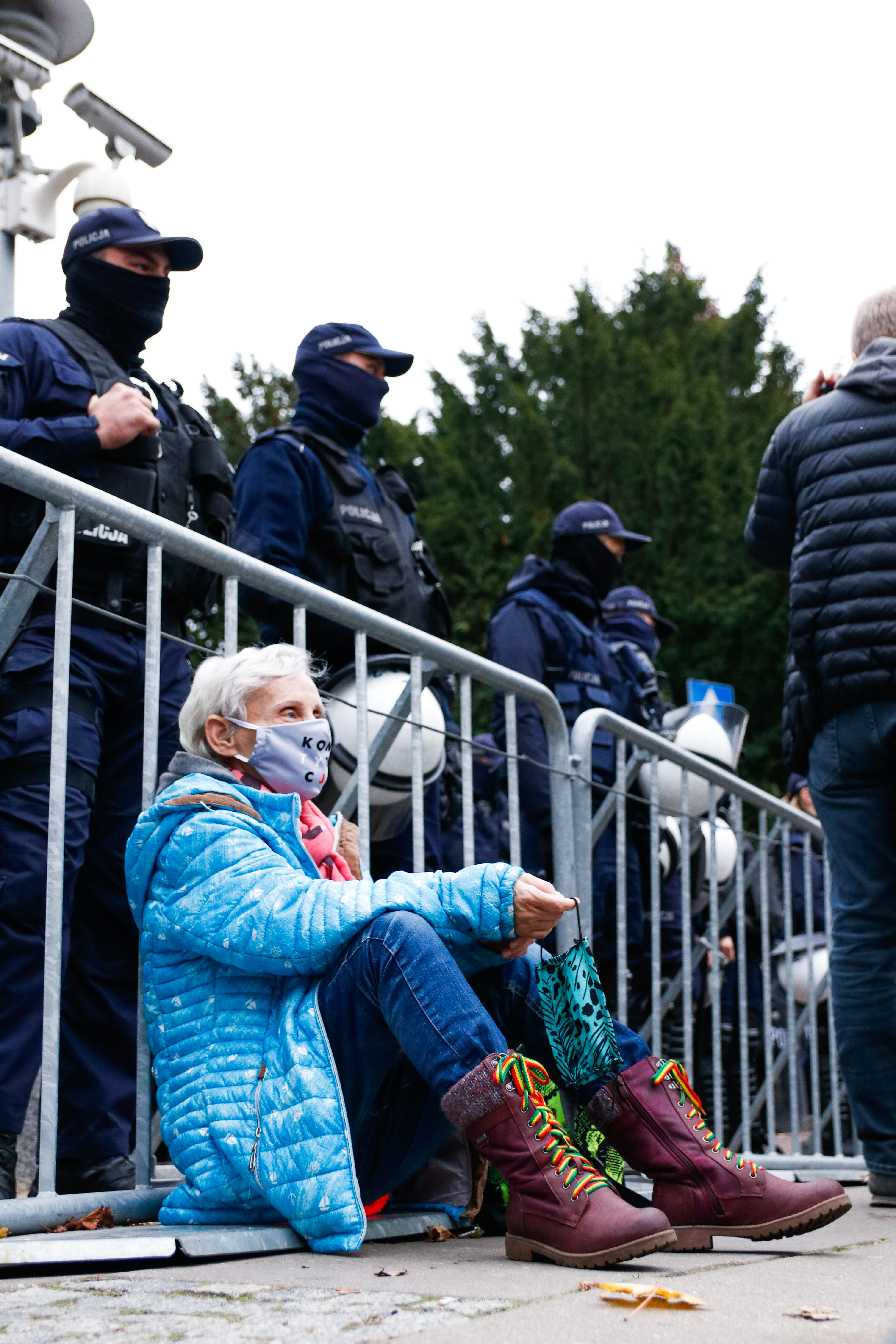 Strajk kobiet - Babcia Basia oparta o barierki obstawione przez policję przed sejmem.